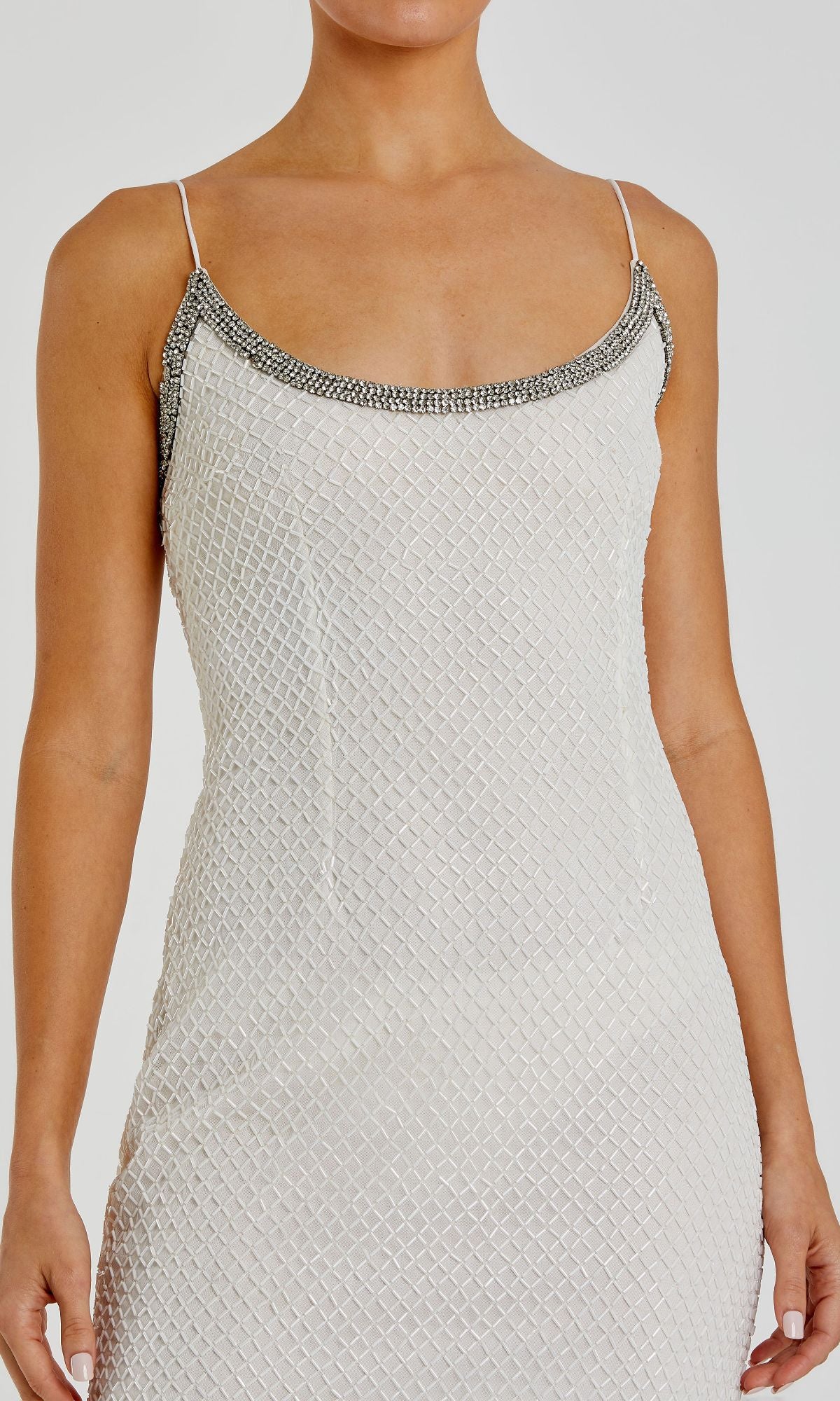 A person wearing the Sleek Long Beaded Prom Dress (Mac Duggal 93551), a sleeveless white gown with geometric texture, thin straps, and silver embellishments along the neckline.